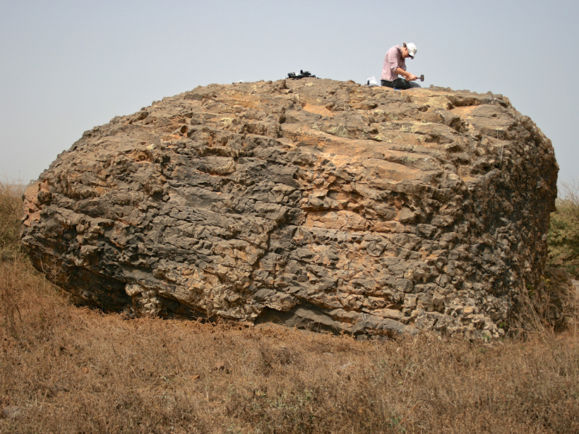A member of a research team hammers the surface of a huge rock on Santiago Island, which lies off the west coast of Africa. The team published new evidence today that an enormous tsunami may have carried this and many other hefty boulders high up onto the island. Credit: Ricardo Ramalho